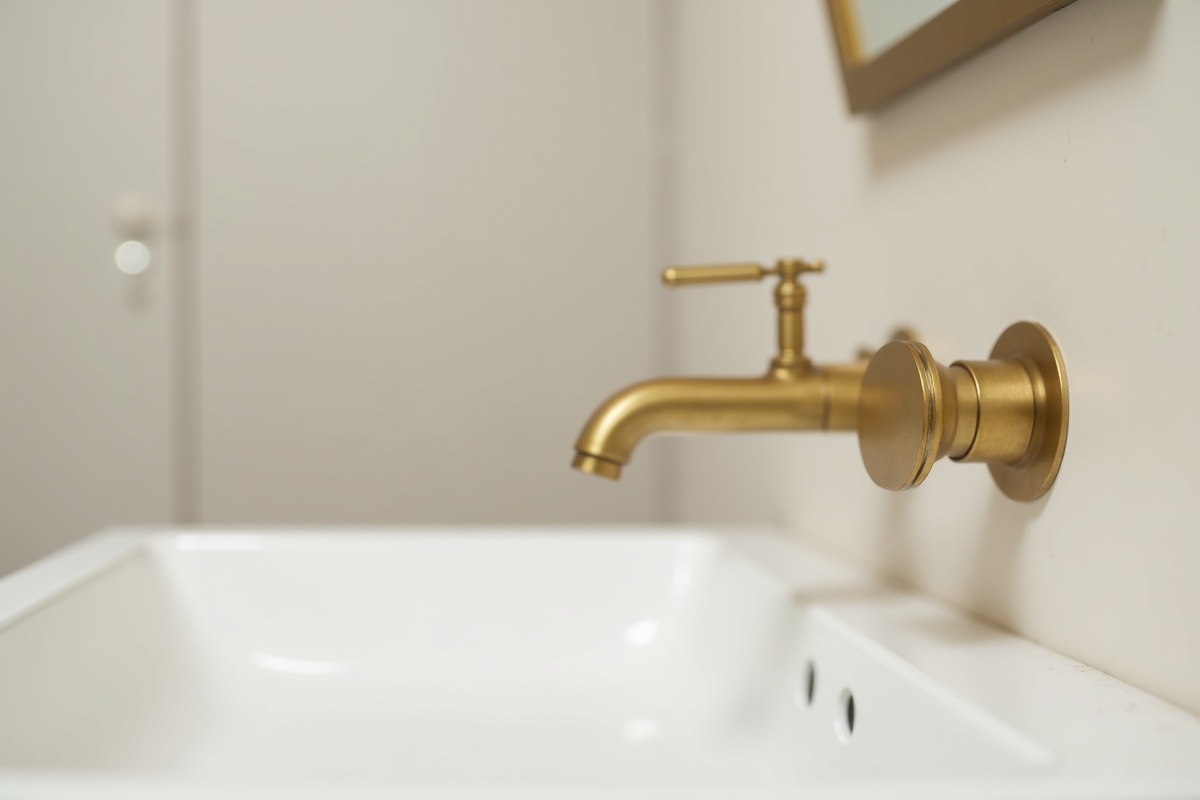 Brushed brass faucet with gold handle detail on white bathroom fixture showing warm metal hardware finish trend in DFW bathrooms for 2026