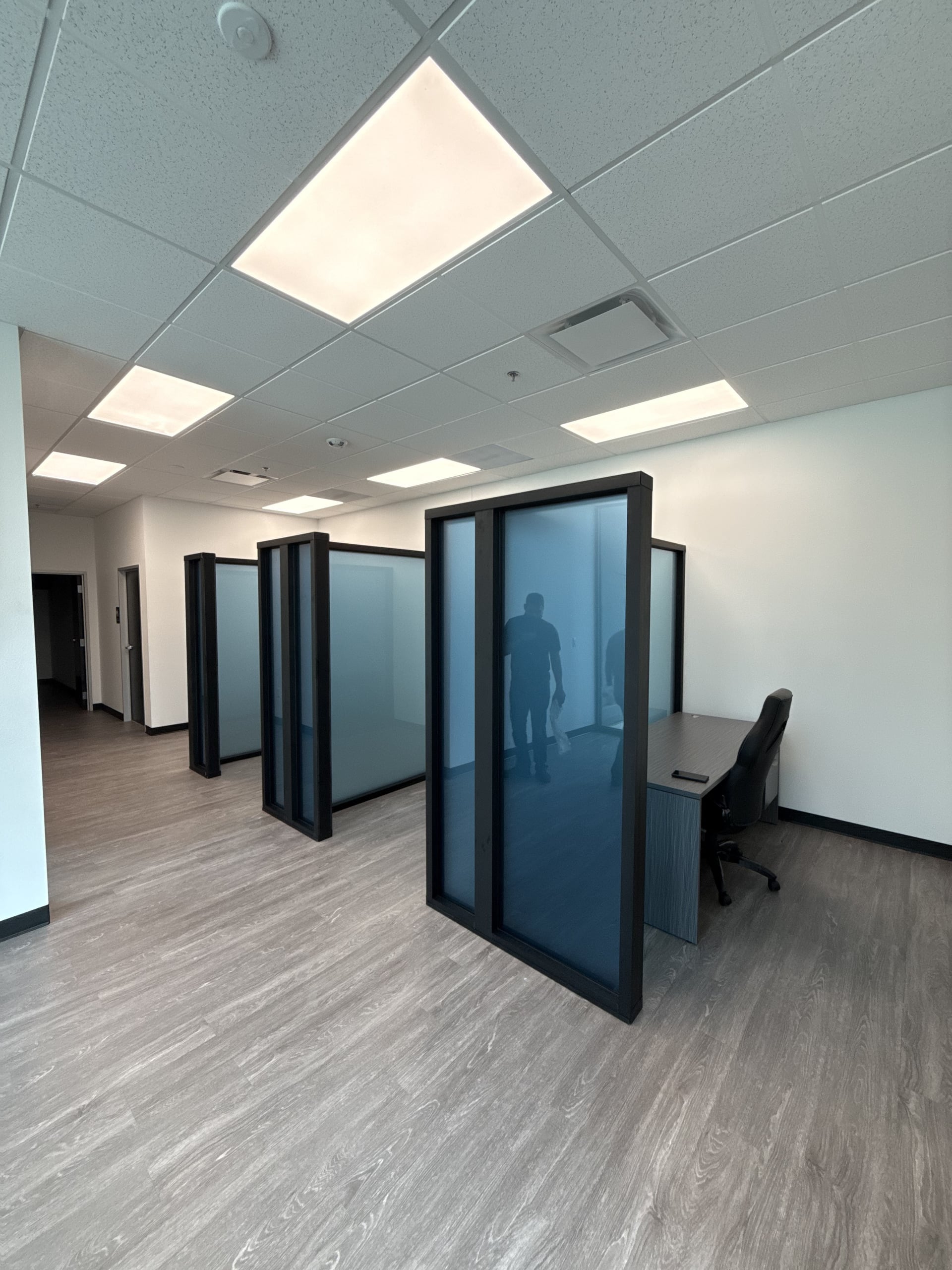 DFW office partition system in use, with a worker visible through blue-tinted glass between aluminum-framed panels