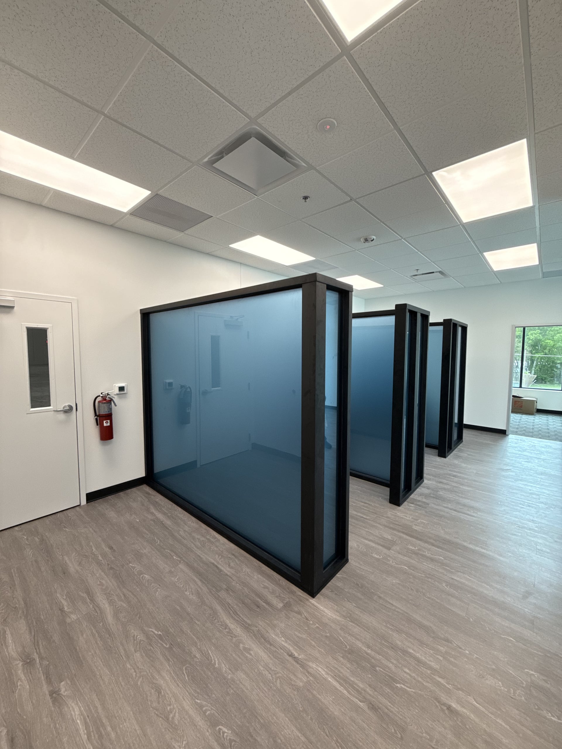 Walkthrough view of aluminum-framed glass partitions with blue-tinted privacy glass forming individual office bays in a DFW workplace